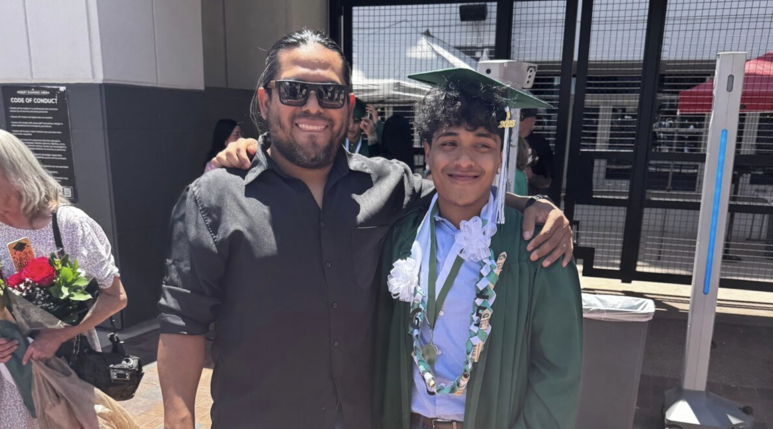 man posing with teenage boy in graduation cap and robe
