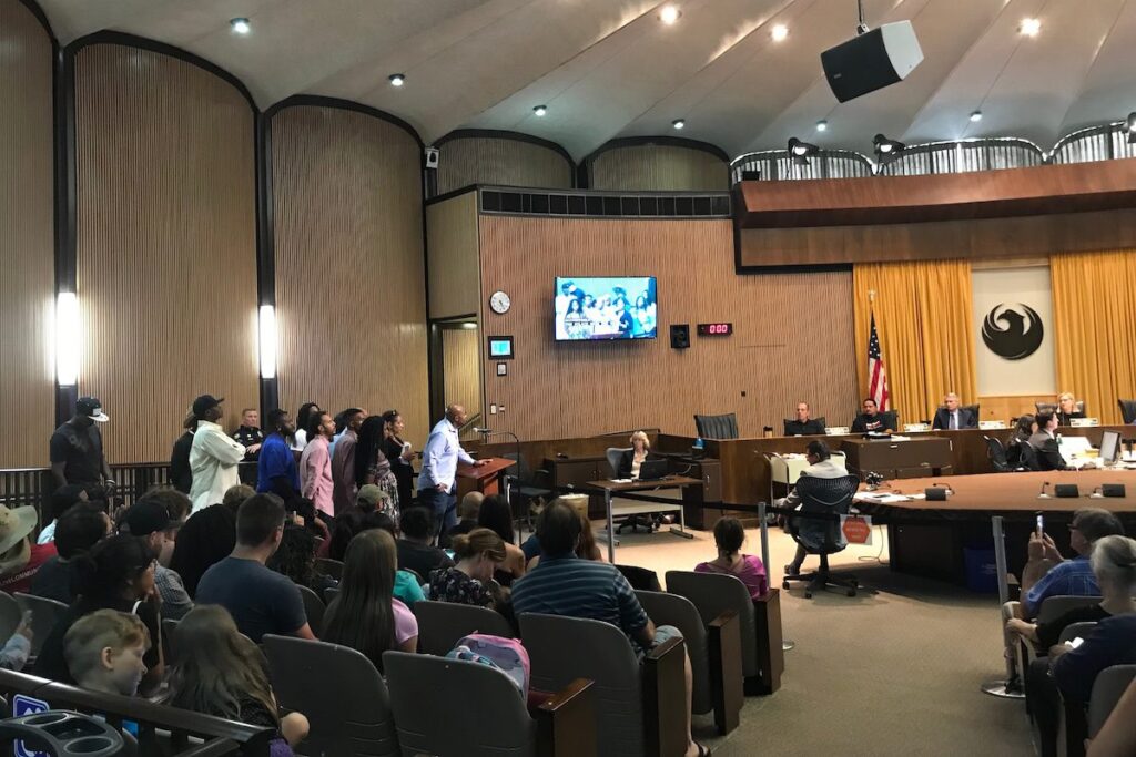 group of people standing behind podium and man speaking into mic in front of City Council