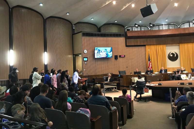 group of people standing behind podium and man speaking into mic in front of City Council