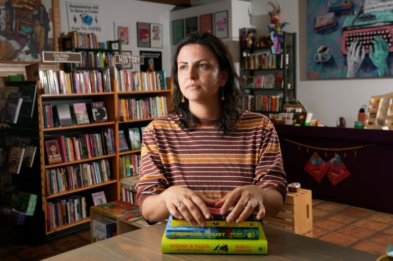 Hispanic woman in a bookstore sitting with her hands on a stack of books