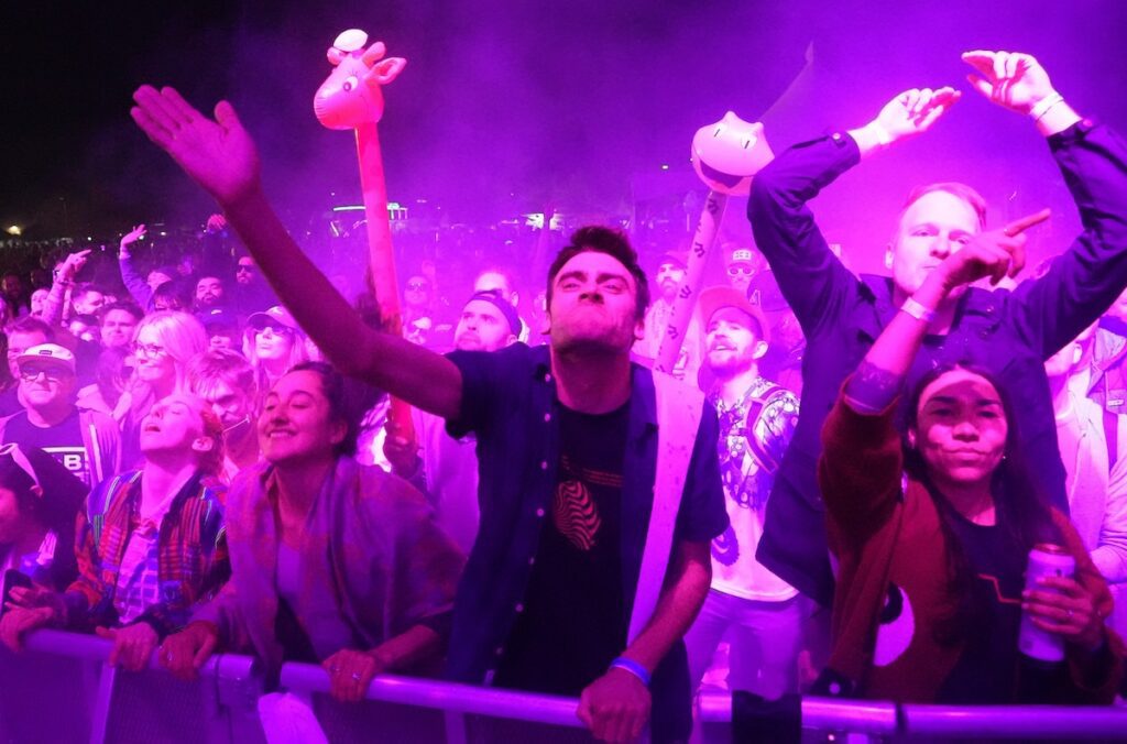 people dancing at the barrier at a concert with a purple light over them