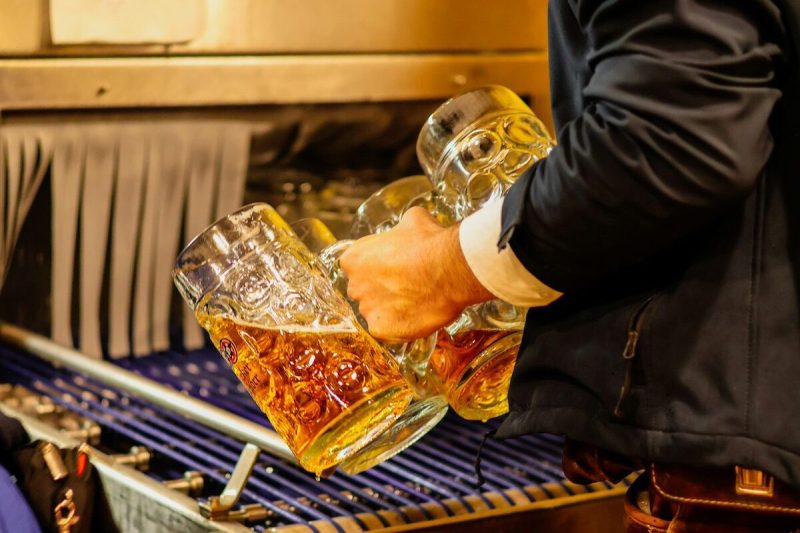 person holding multiple steins up to a spout and pouring beer into them
