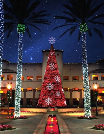 a lit up red Christmas tree in between poles with green Christmas lights