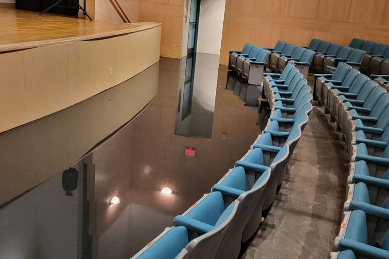 a stage and the first two rows of seating with a large amount of water pooled between the stage and first row