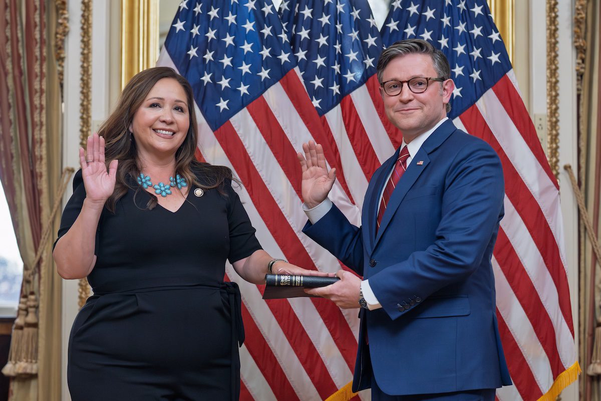 Adelita Grijalva posing with one hand up and one hand on a book next to Mike Johnson, posing with one hand up