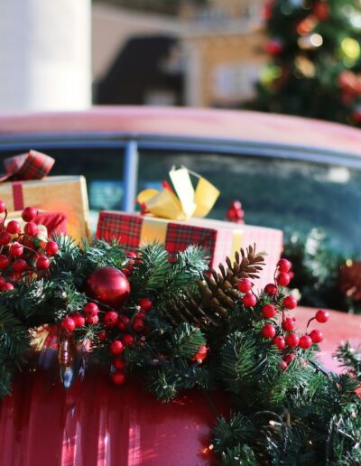 Christmas decorations on a red car with an outdoor Christmas tree in the background