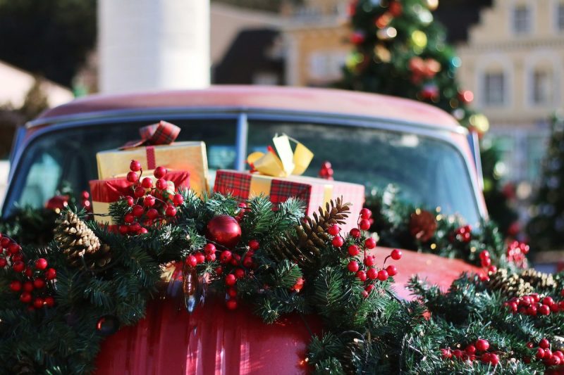Christmas decorations on a red car with an outdoor Christmas tree in the background