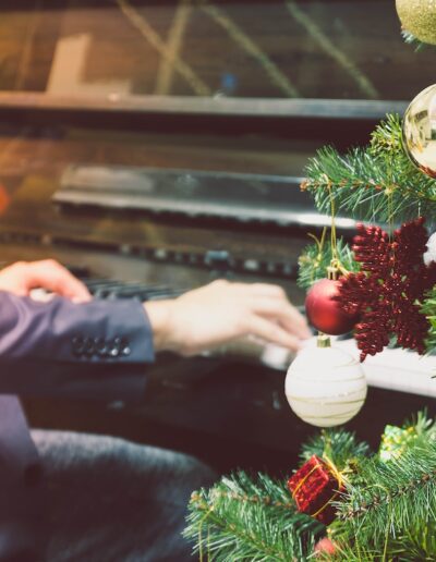 person playing the piano next to a Christmas tree