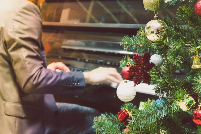 person playing the piano next to a Christmas tree