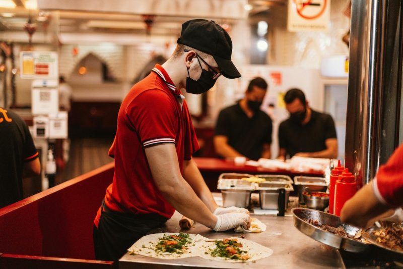 man wearing fast food uniform and mask rolling wraps