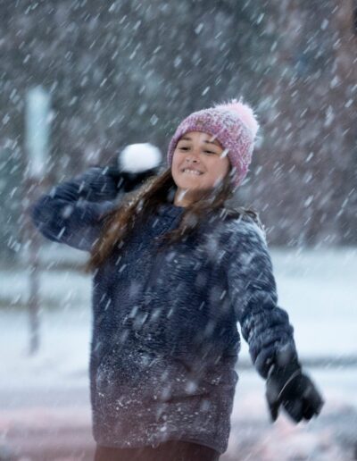 girl throws a snowball while it is snowing outside