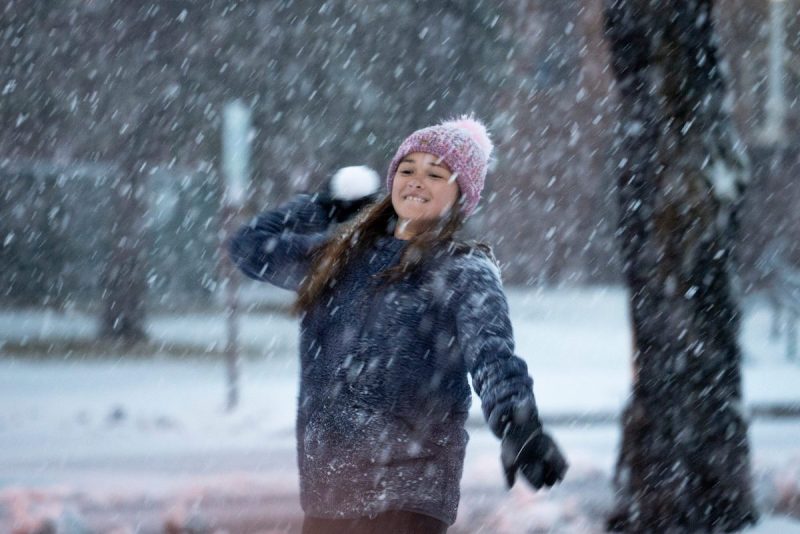 girl throws a snowball while it is snowing outside
