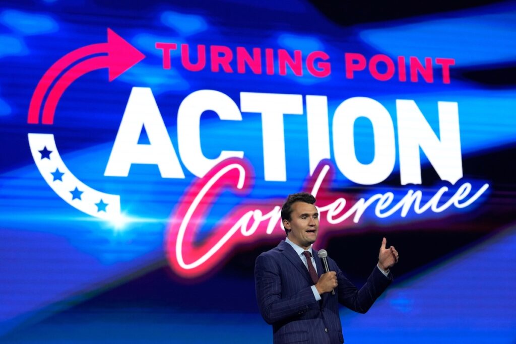 Charlie Kirk speaking in front of screen that says Turning Point Action Conference