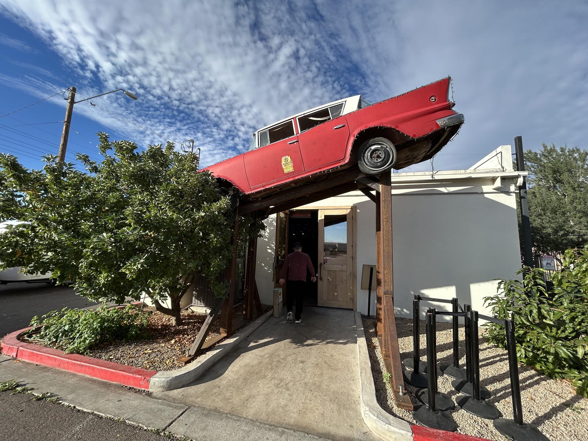 a classic car suspended over the entrance to a small building