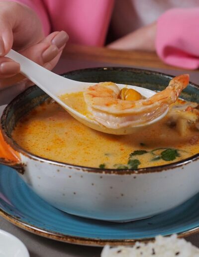 someone holding up a spoon with a shrimp on it above a bowl or orange soup