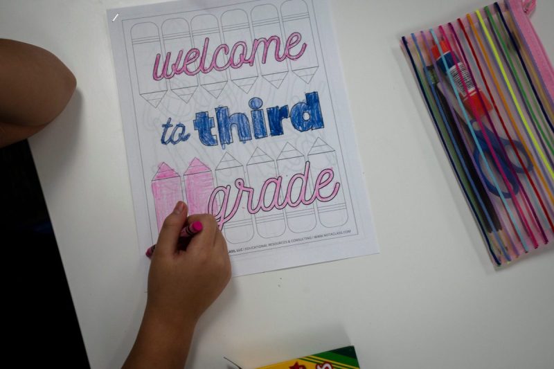 hand coloring in a paper that says "welcome to third grade" on a desk