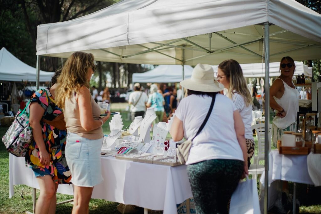people looking at a vendor tent displaying jewelry at an outdoor market