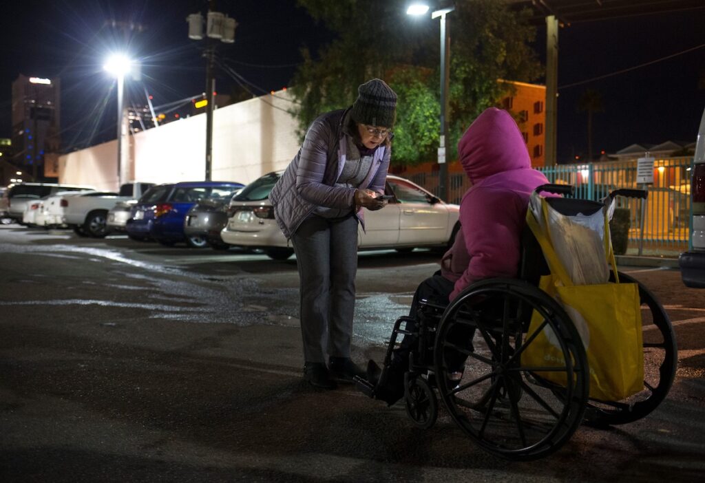 a woman speaking to another woman in a wheelchair in a parking lot