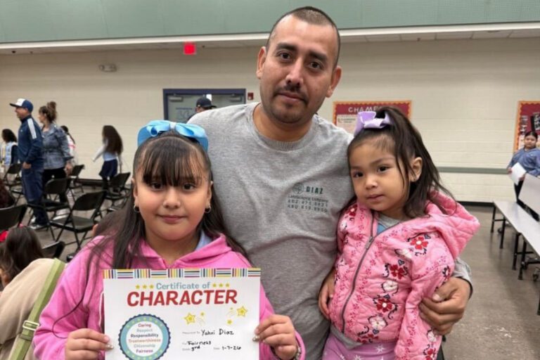 man standing with two little girls, one holding a certificate of character award