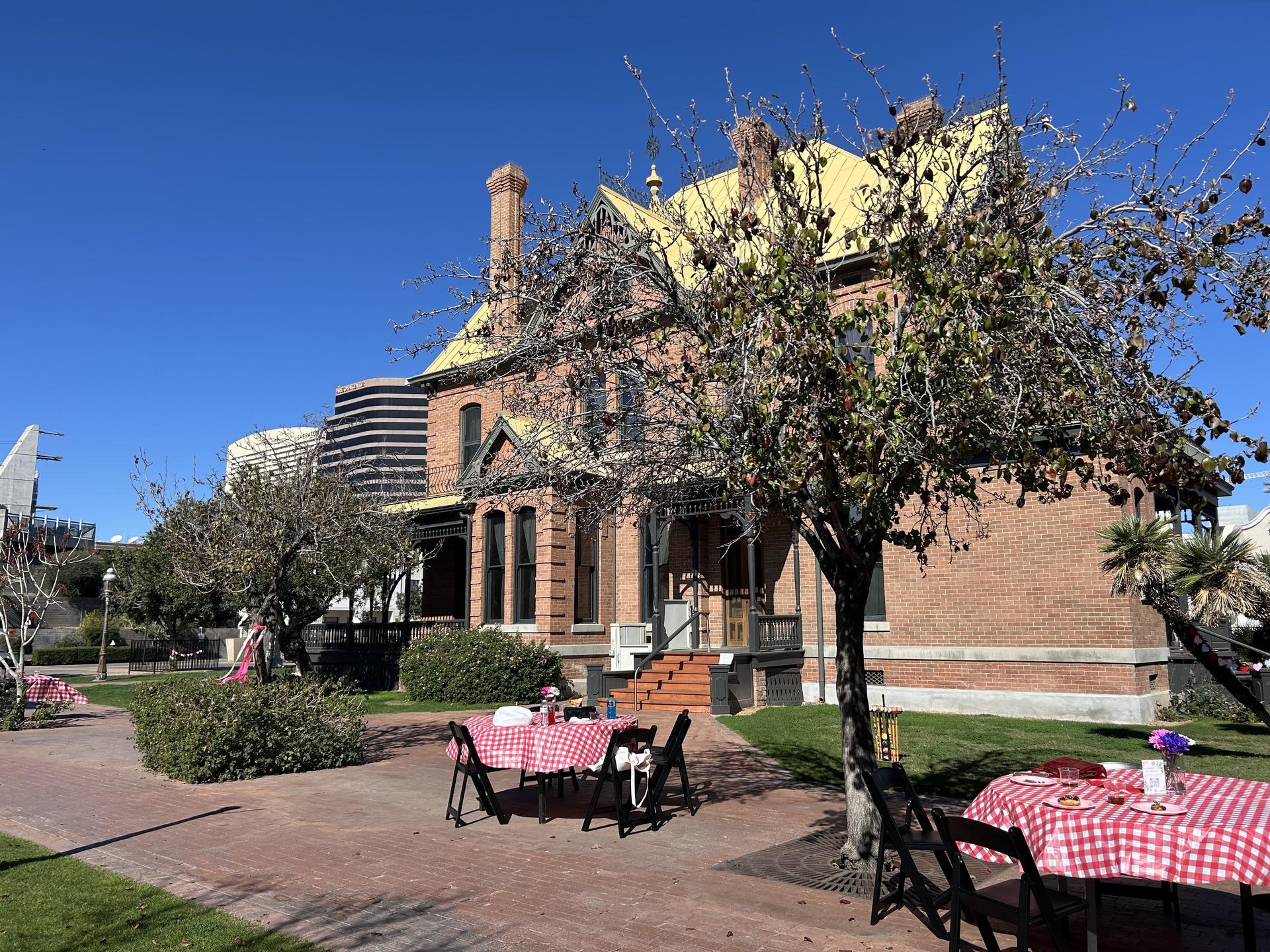 tables and chairs with checkered tablecloths next to a large brick house
