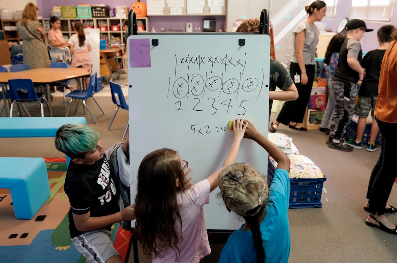 students work on a math problem on a white board in a classroom