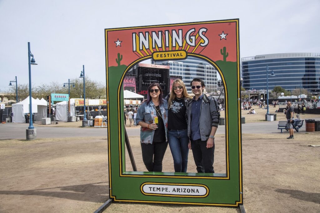 people posing inside of a stand that says Innings Festival Tempe Arizona