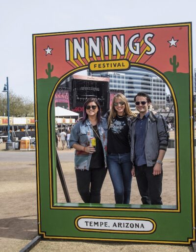 people posing inside of a stand that says Innings Festival Tempe Arizona