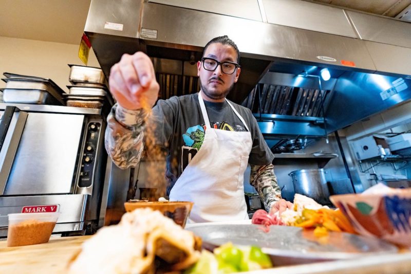man sprinkling seasoning on a plate in a kitchen