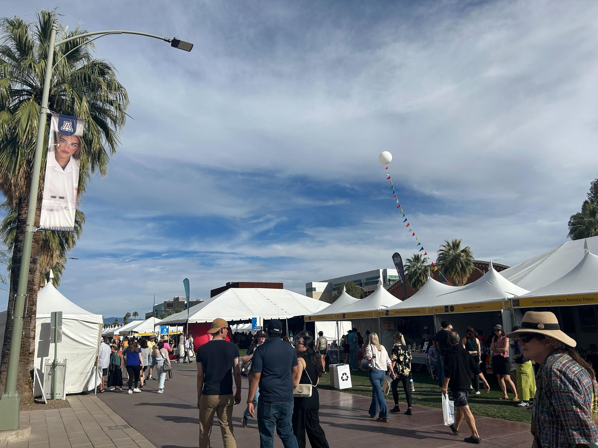 outdoor festival with crowds of people walking on path with white sides of both sides