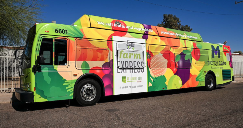large bus printed with bright green designs and brightly colored fruits and veggies and text that says Farm Express