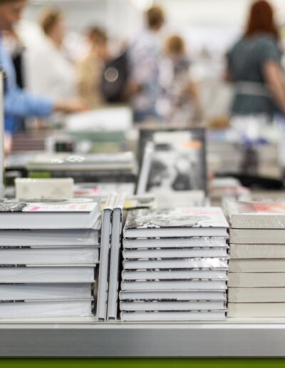 people walking past tables with stacks of books on them