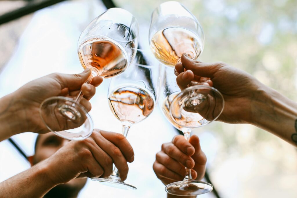four hands holding wine glasses toasting them together
