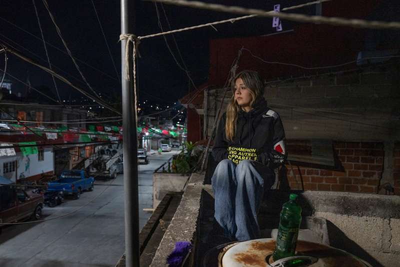 woman sits on a roof, sadly overlooking a street