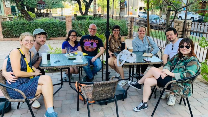 a group of eight people seated at a patio table smiling at camera