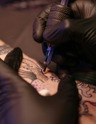 close up of gloved hands tattooing a design on a person's arm