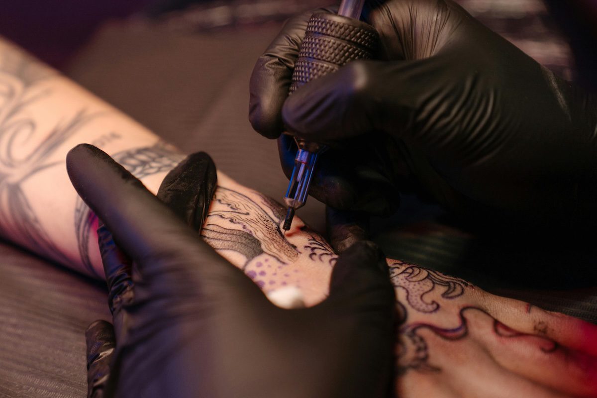 close up of gloved hands tattooing a design on a person's arm