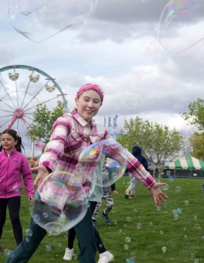 three kids running around at a fair chasing bubbles