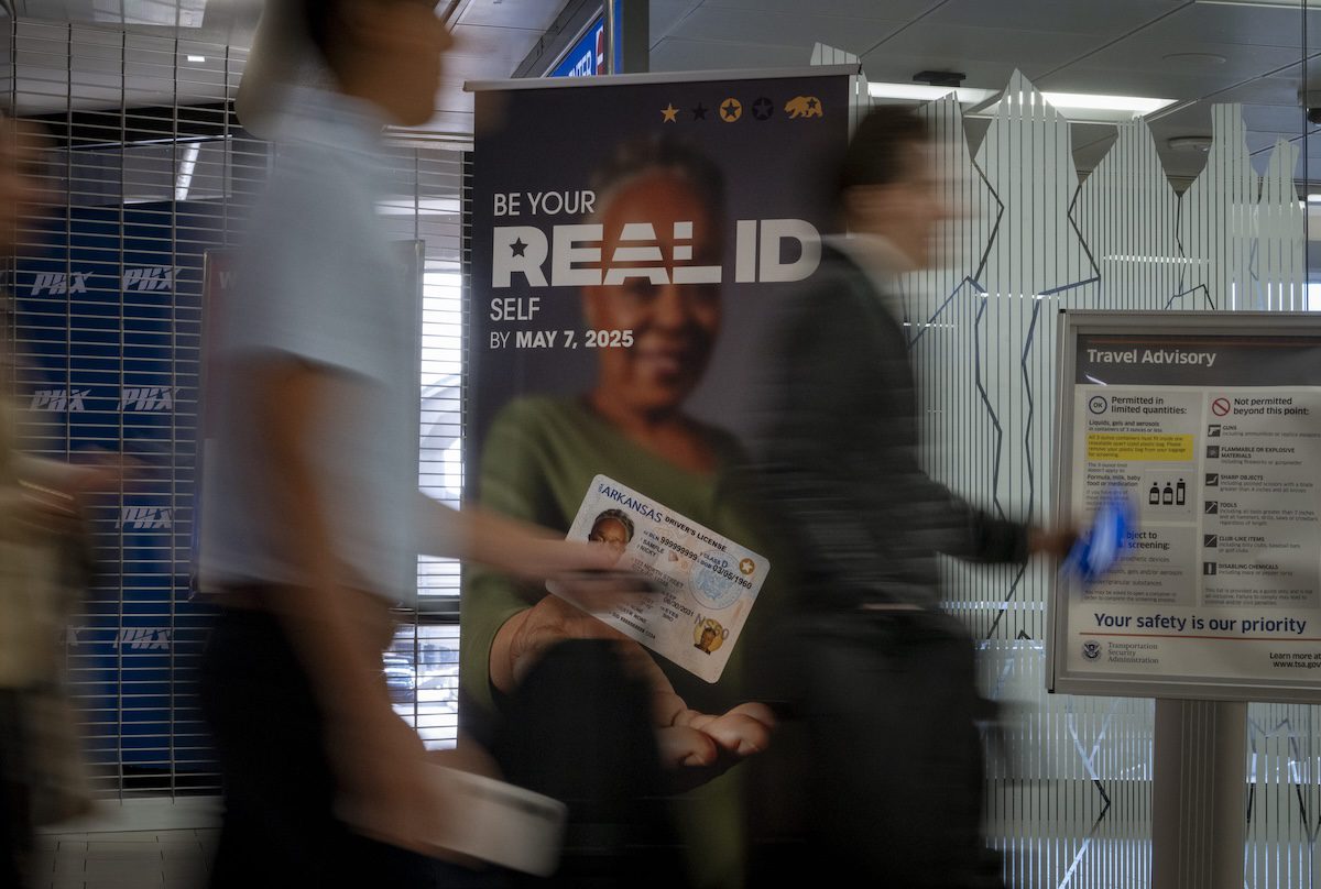 people walk past a Real ID sign in an airport