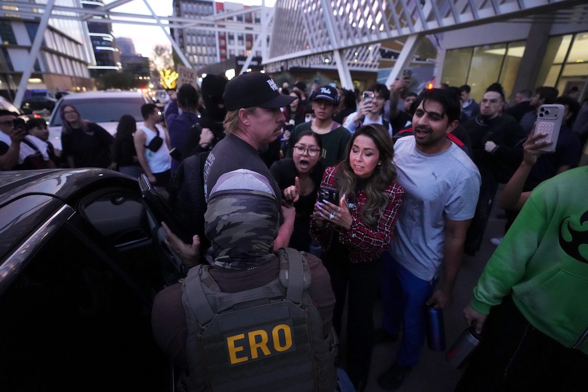 protestors crowding ice agents outside a building and car