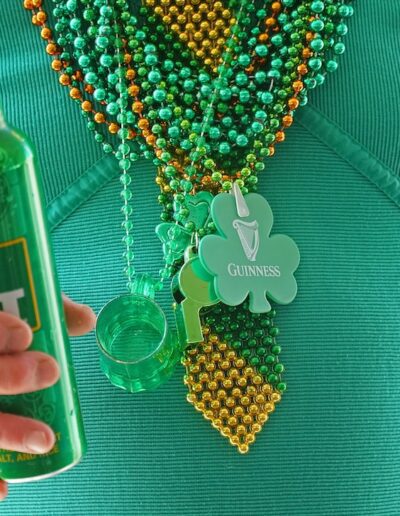 close up of man wearing green shirt and beads holding a green beer