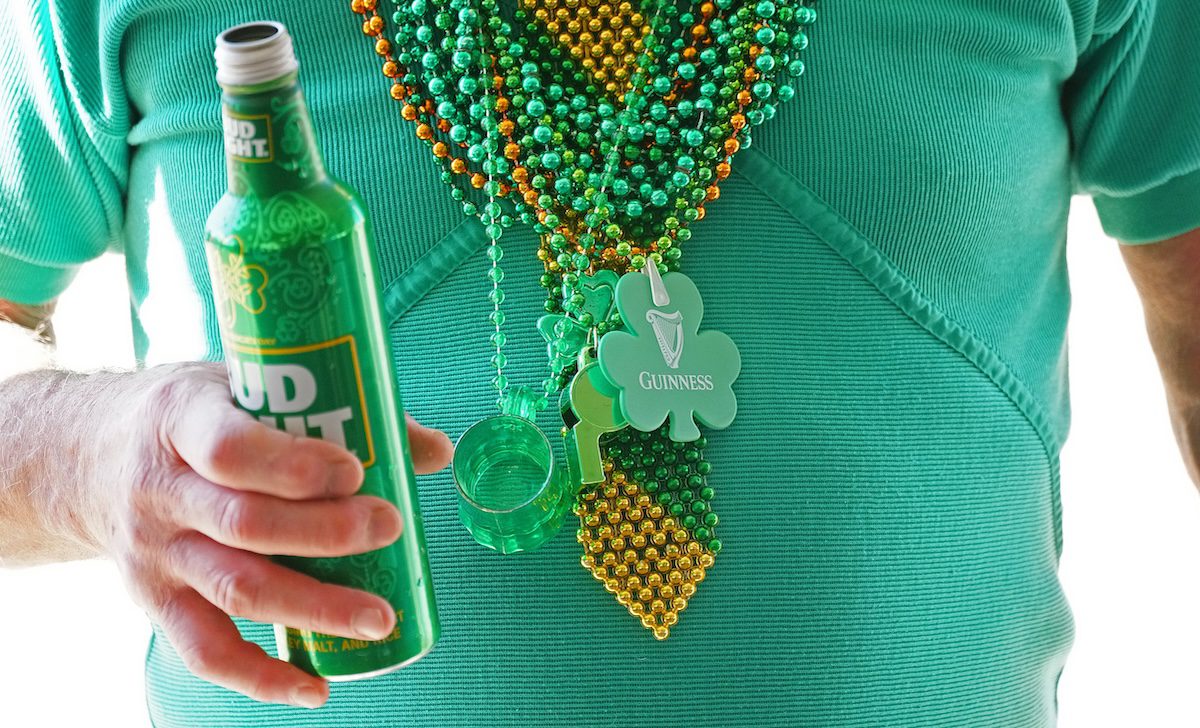 close up of man wearing green shirt and beads holding a green beer
