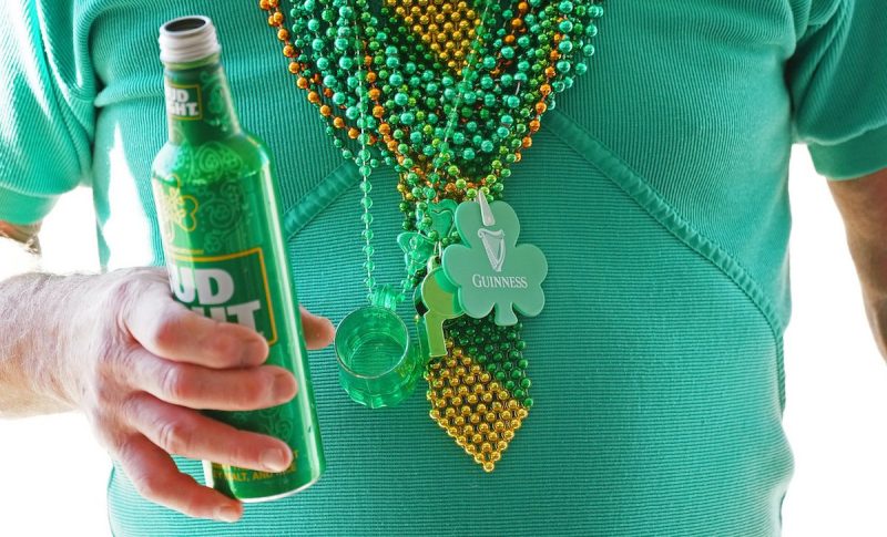 close up of man wearing green shirt and beads holding a green beer