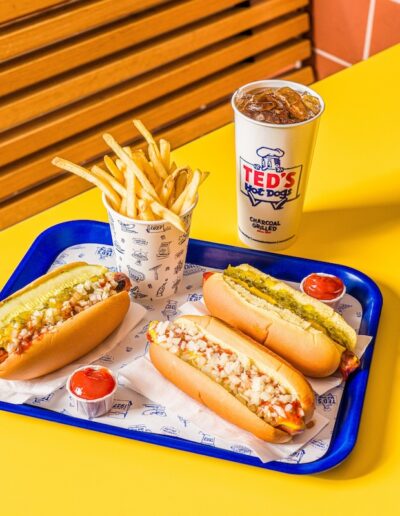 a tray on a table with three hot dogs, a cup of fries, and a soda