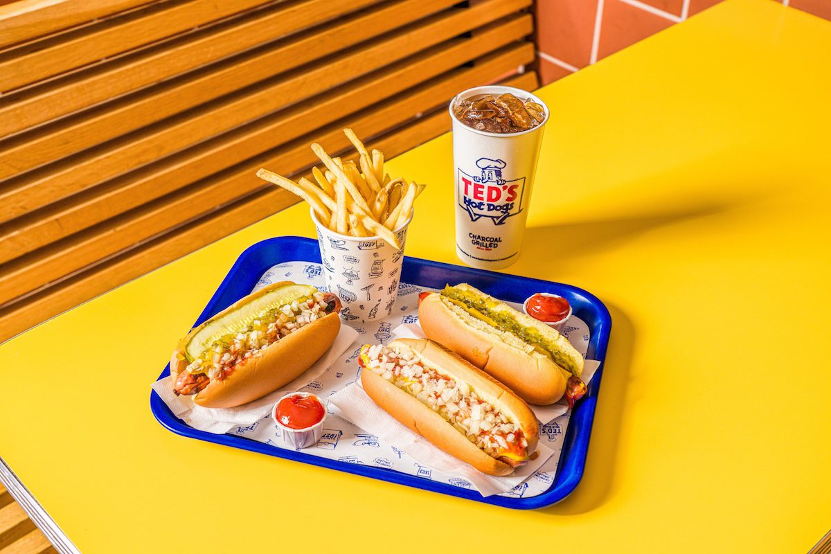 a tray on a table with three hot dogs, a cup of fries, and a soda