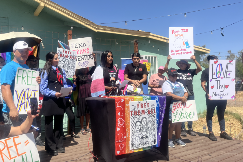 group of people holding posters around person speaking at podium