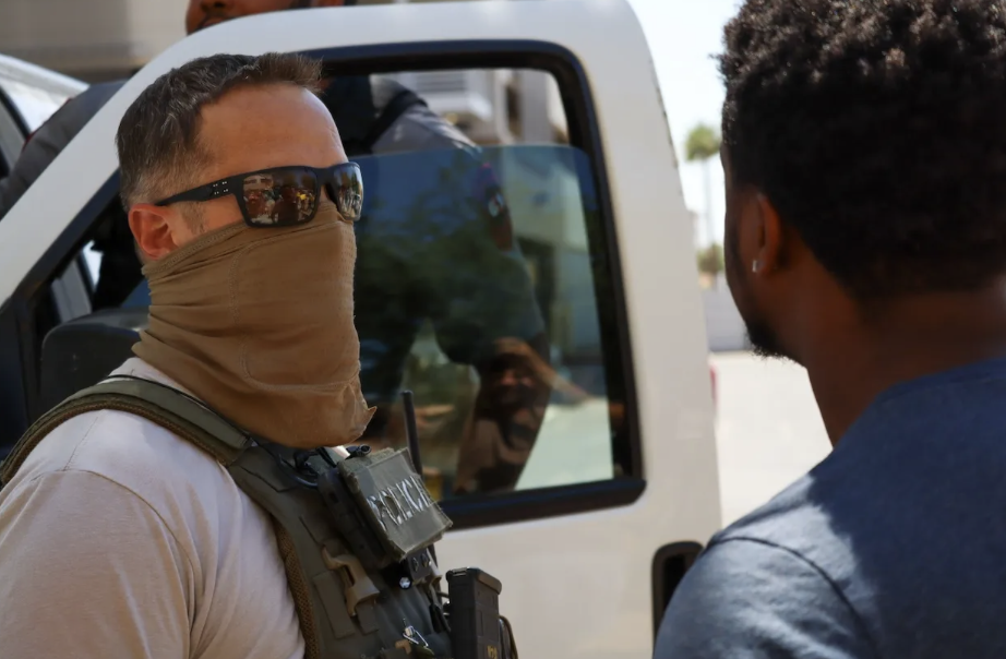 ice agent wearing sunglasses and a mask facing another man