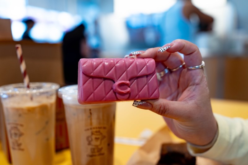 hand holding a bright pink mini coach bag in front of coffee cups