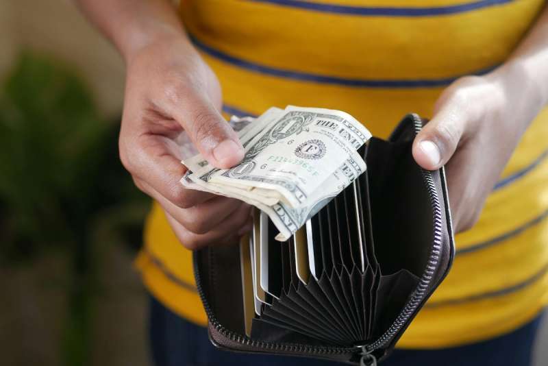 two hands holding an open wallet with a few dollar bills in it