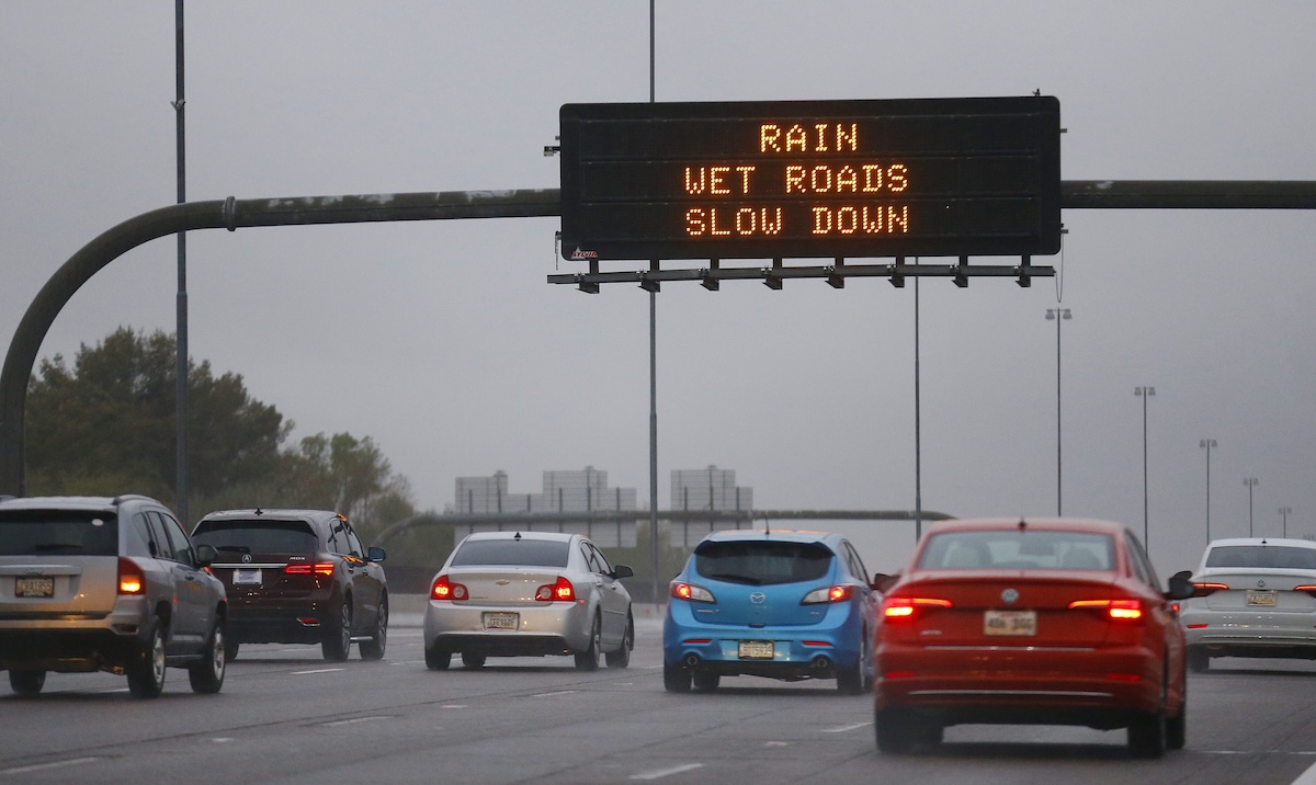 cars on the freeway below an overhead sign that says rain wet roads slow down