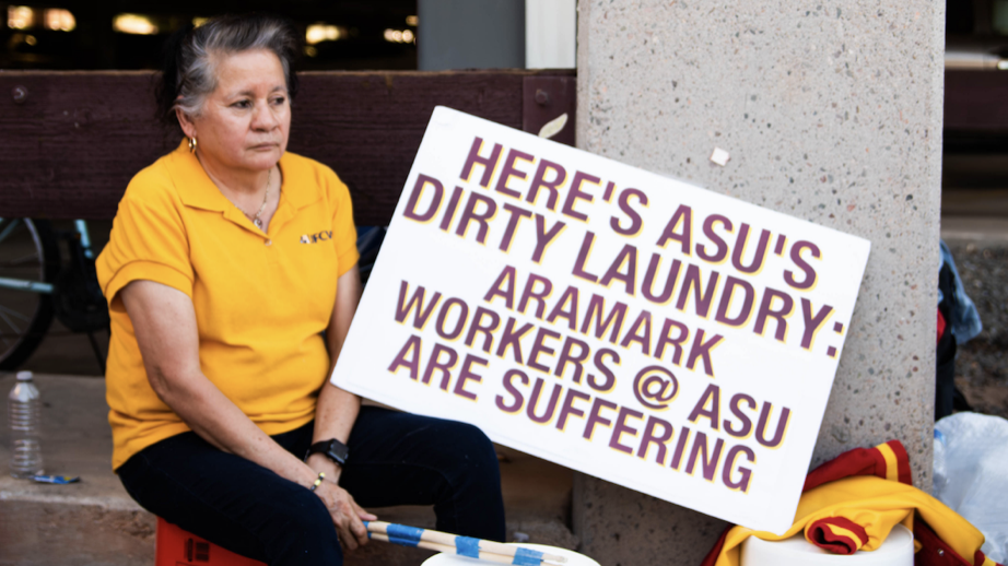 woman wearing yellow ASU polo sitting next to a sign that says Here's ASU's dirty laundry: Aramark workers @ ASU are suffering